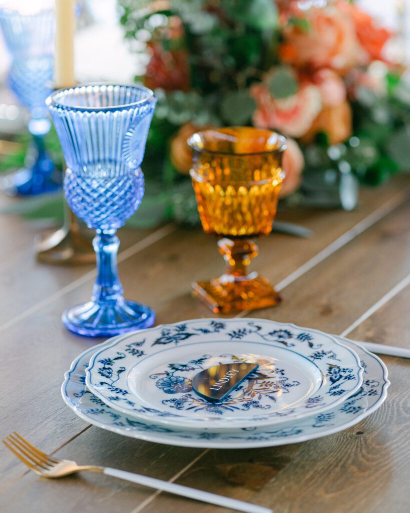 Wedding table setting with blue and amber glassware, blue and white floral plates, and autumn floral centerpiece.