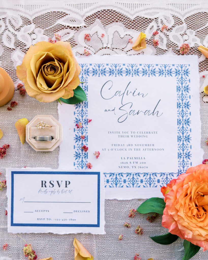 Wedding invitation suite with blue floral border, RSVP card, engagement ring in velvet box, and yellow roses.