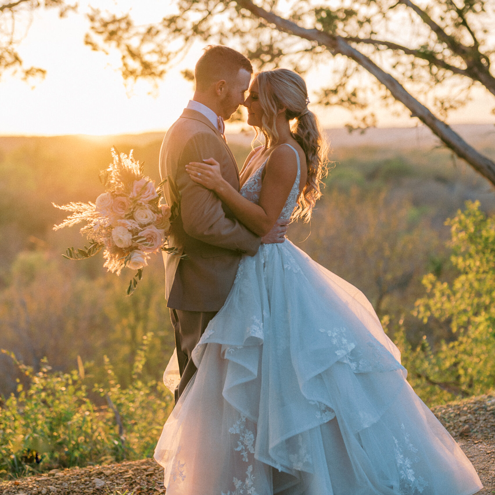 Newlywed couple embracing at sunset in an outdoor wedding setting in Fort Worth Texas with bride in a lace dress and groom in a beige suit.